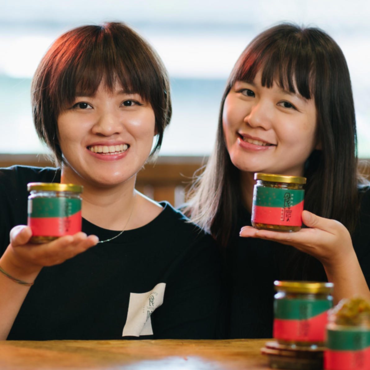 兩名女人拿著裝辣椒醬的罐子，對著鏡頭微笑