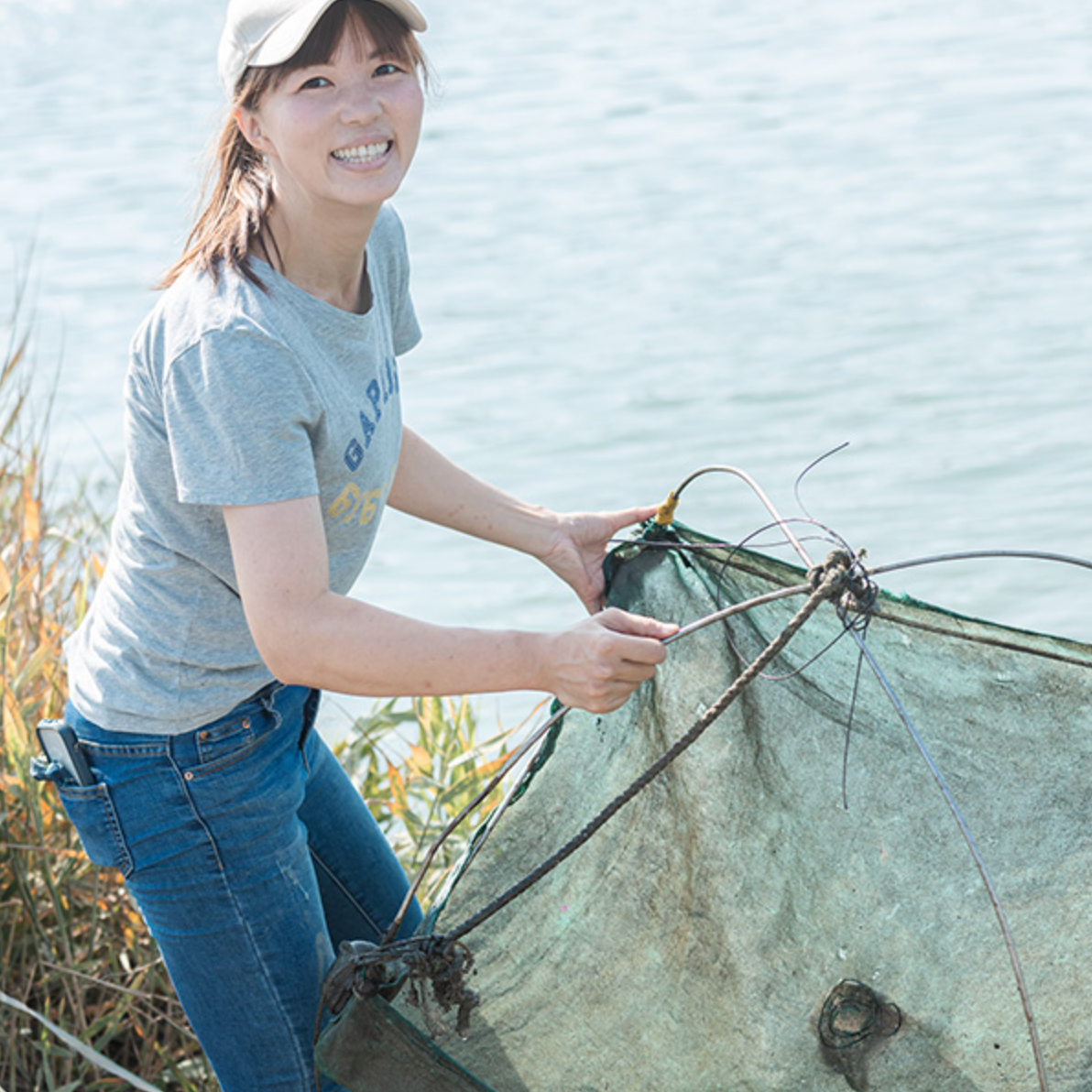 一名女性拿著漁網站在魚塭前