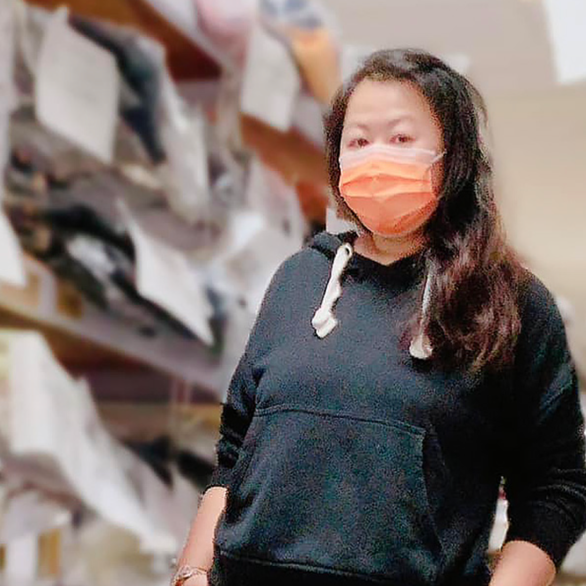 一位身穿黑色連帽上衣、戴著橘色口罩的女性