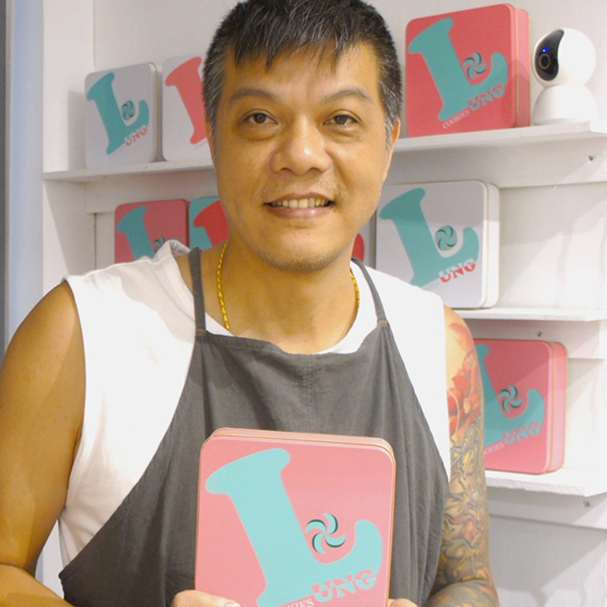 一位穿著圍裙的男性，拿著一個粉紅色的盒子，上面有他的餅乾品牌LOGO