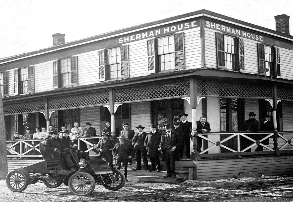 A black and white photo of a sherman house with a car parked in front of it.