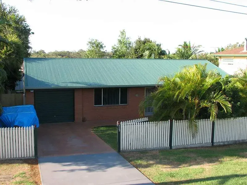 A brick house with a green roof and a white picket fence