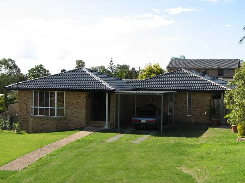 A car is parked under a canopy in front of a brick house