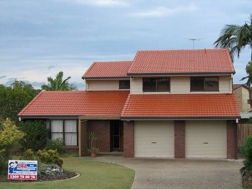 A house with a red tiled roof has a for sale sign in front of it