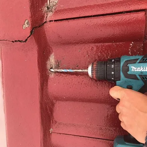 A person is using a makita cordless drill to drill a hole in a red wall.