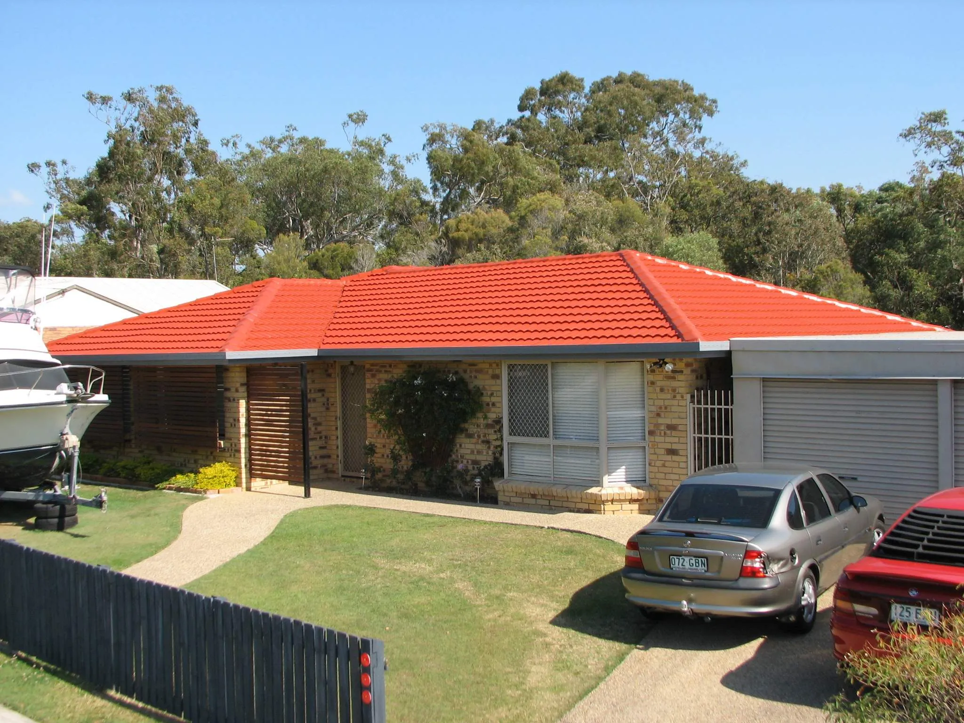 Two cars are parked in front of a house with a red roof