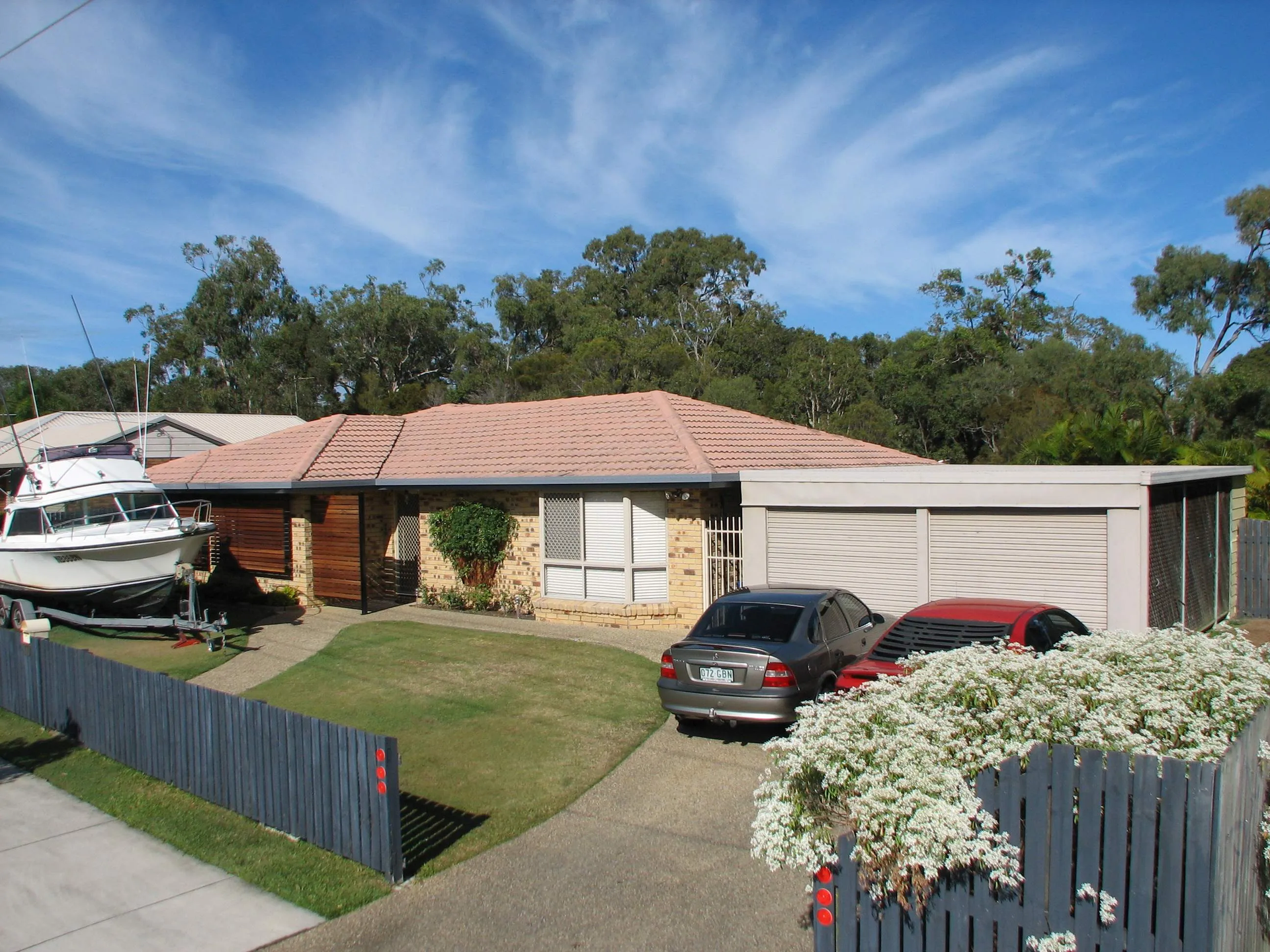 Two cars are parked in front of a house with a boat in the garage