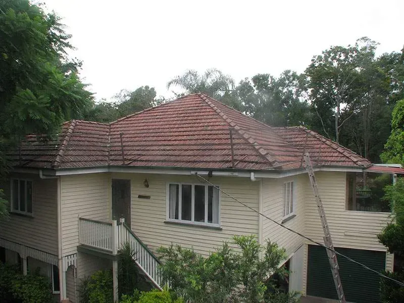 A white house with a red tiled roof is surrounded by trees