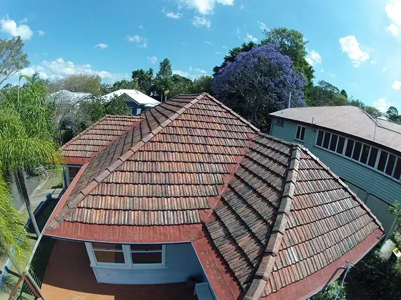 An aerial view of a house with a tiled roof and trees in the background.