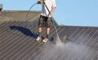 A man is cleaning the roof of a building with a high pressure washer.