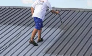 A man is painting a metal roof with a sprayer.