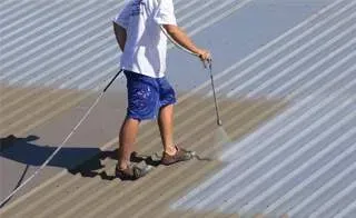 A man is painting a metal roof with a sprayer.