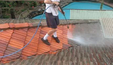 A man is cleaning a tiled roof with a high pressure washer.