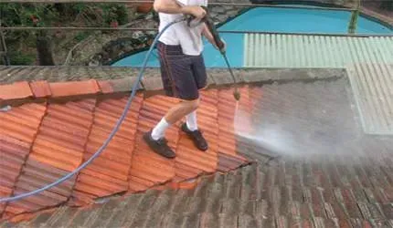 A man is cleaning a tiled roof with a high pressure washer.