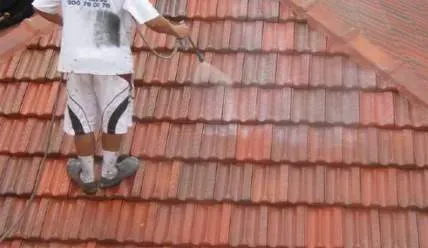 A man is cleaning a tiled roof with a high pressure washer.
