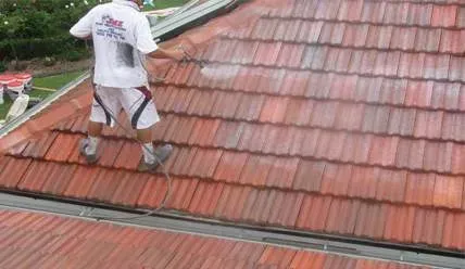 A man is standing on top of a tiled roof cleaning it.