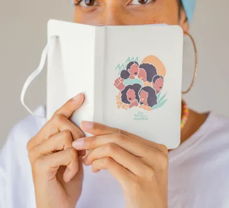 Uma mulher está segurando um caderno na frente do rosto.