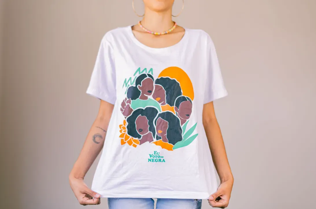 Uma mulher está vestindo uma camiseta branca com a imagem de um grupo de pessoas.