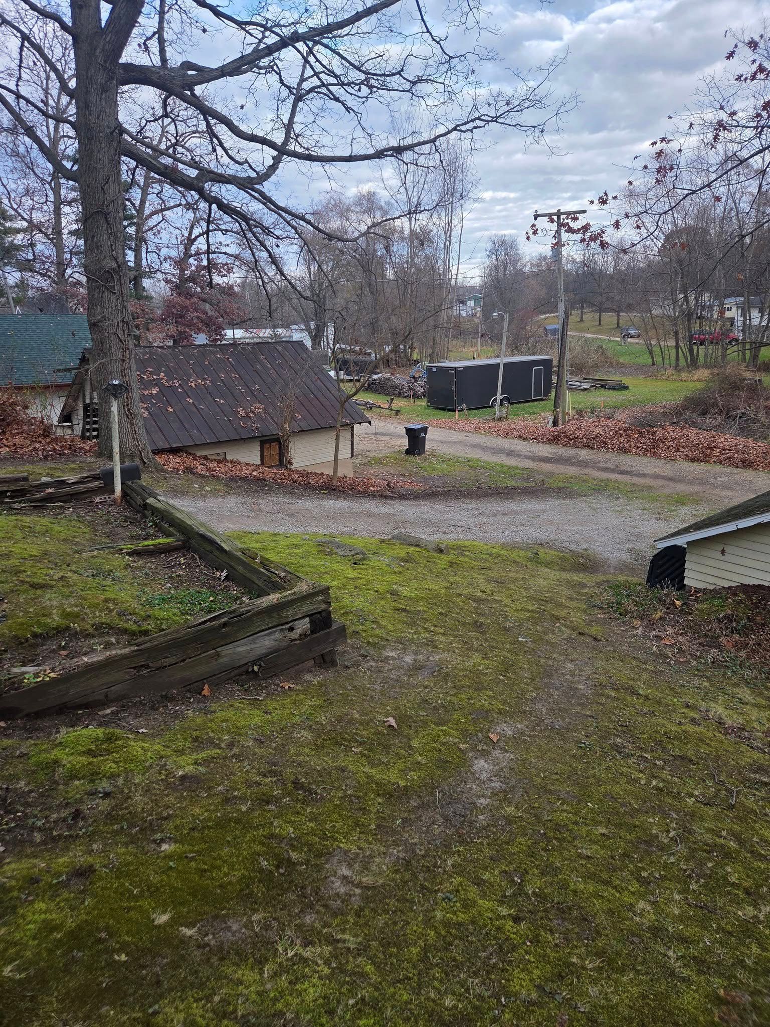 Dirt road through a small, rural area with multiple low buildings and scattered autumn leaves.