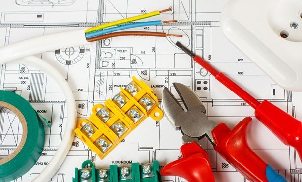 Man in safety glasses using pliers on electrical wiring next to brick wall.