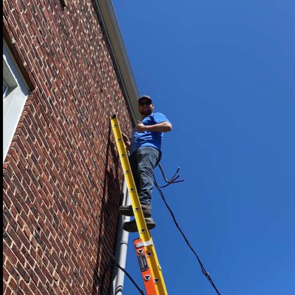 Man on a yellow ladder against a brick building under a blue sky.