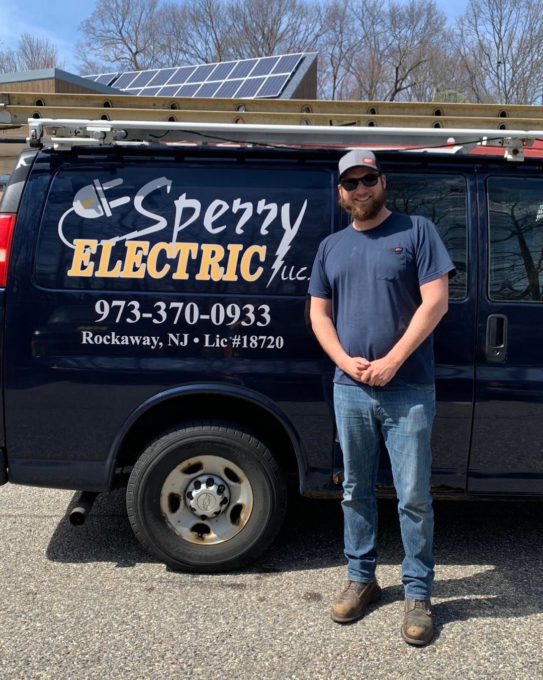 Man standing by a dark blue Sperry Electric van in Rockaway, NJ; solar panels on roof.