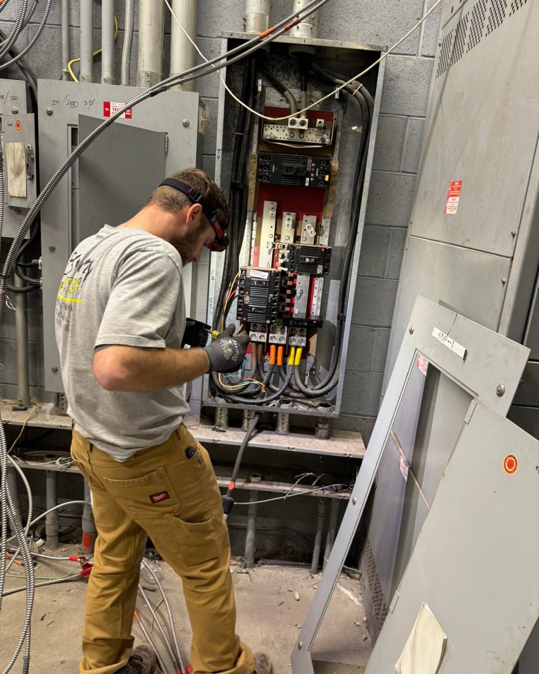 Electrician working on a panel in a utility room, wearing safety glasses and gloves.