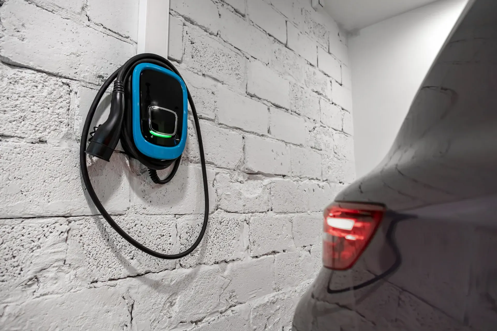 Electric vehicle charging station on a white brick wall next to a car.