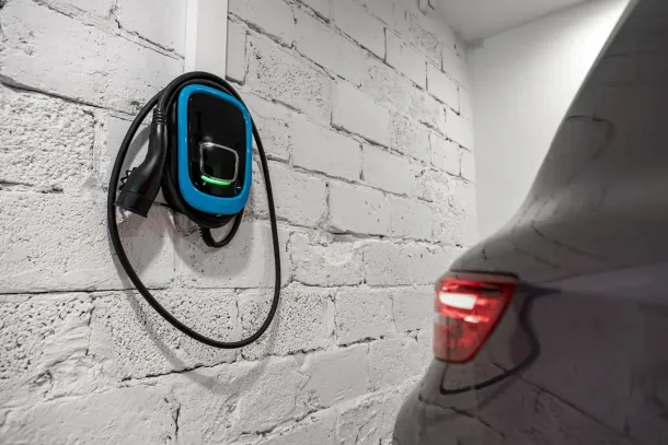 EV charger mounted on a white brick wall, plugged into a grey car's rear.
