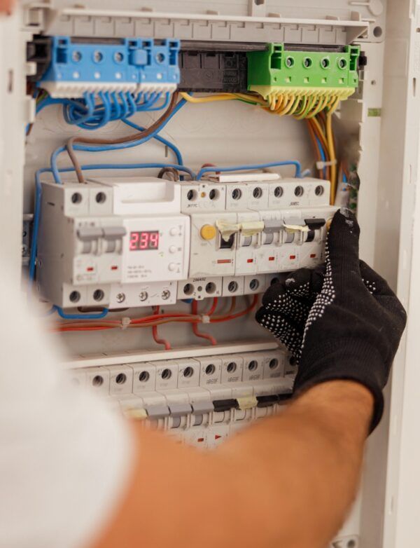 Hand in a black glove near an open electrical panel with wires and circuit breakers.