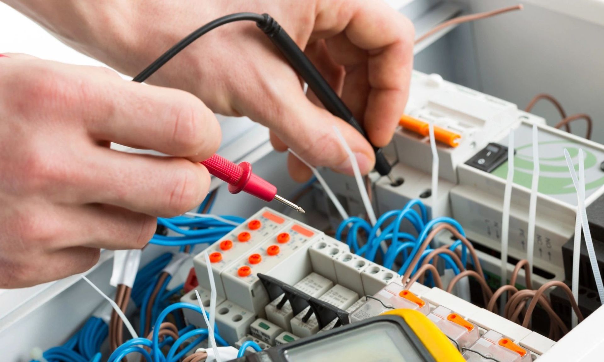 Electrician testing wires in a control panel with a multimeter, hands close up.