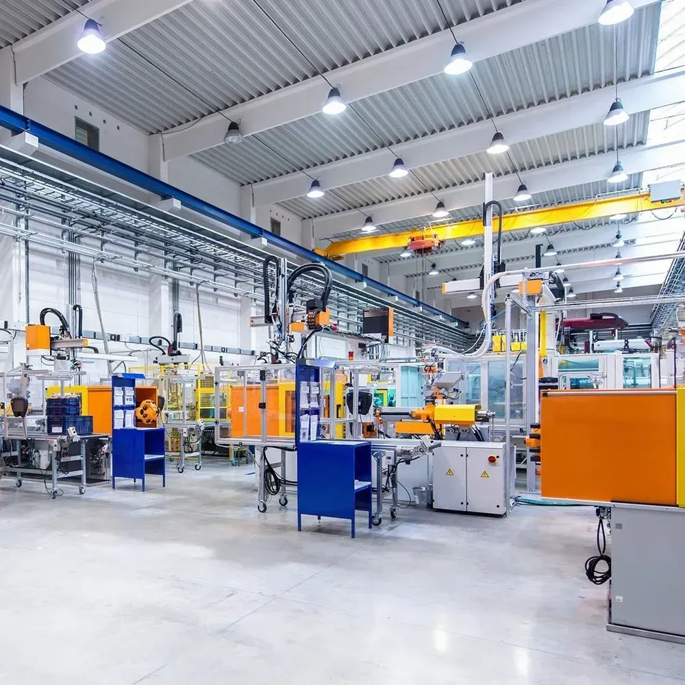 Factory interior with machinery, robots, and overhead lights. White, blue, and orange equipment.