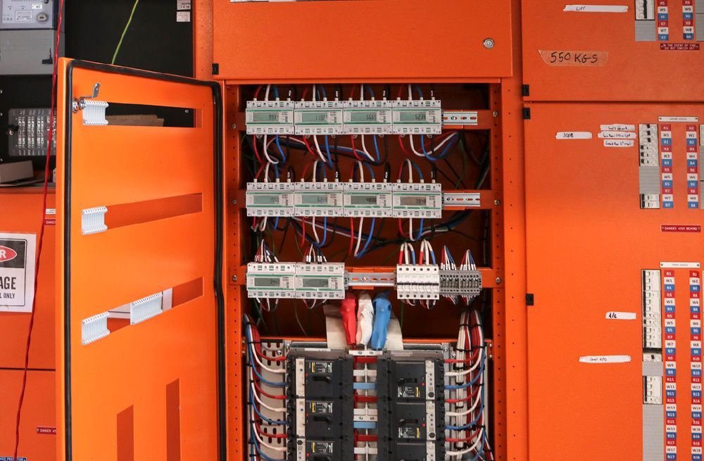 Orange electrical panel with open door, exposing rows of meters and wiring.