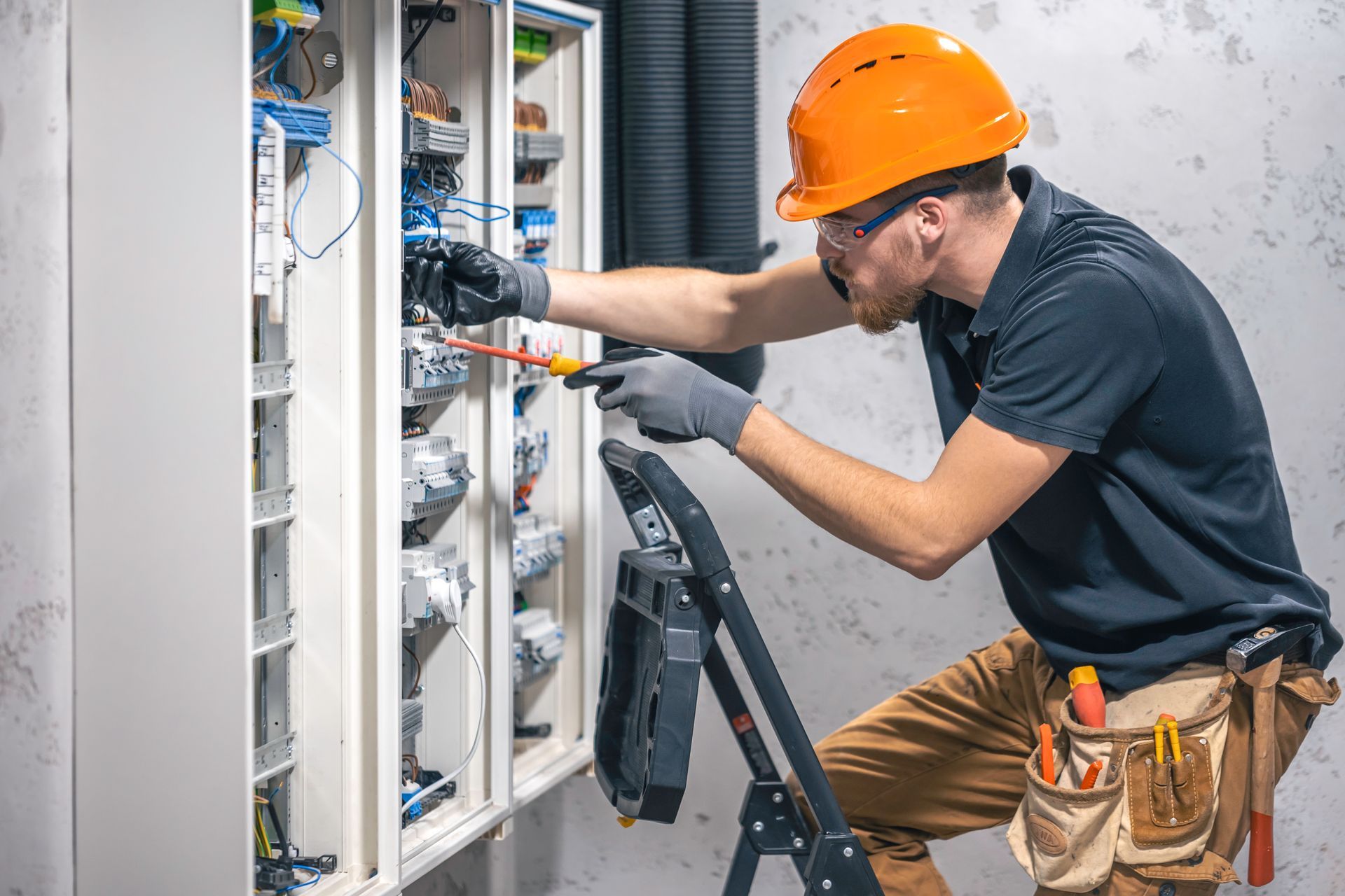 Electrician working on a panel in a utility room, wearing safety glasses and gloves.