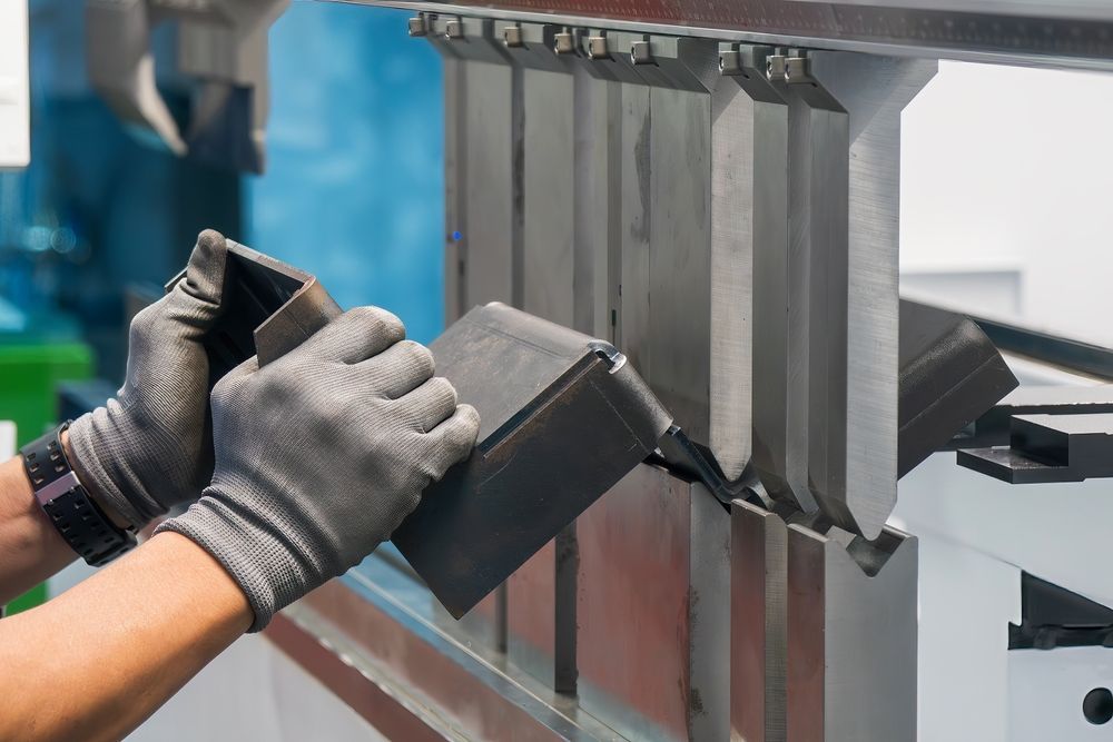 Hands in gloves bending metal using a press brake machine.