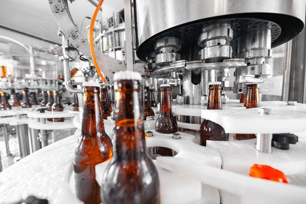 Bottling machine filling brown beer bottles with caps in a brewery.