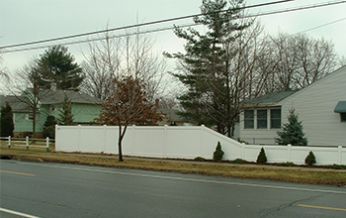 A white fence surrounds a house on the side of the road.