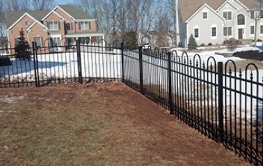 A black metal fence surrounds a snowy yard in front of a house