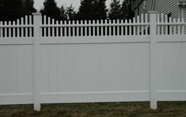 A white vinyl fence is sitting in the grass in front of a house.