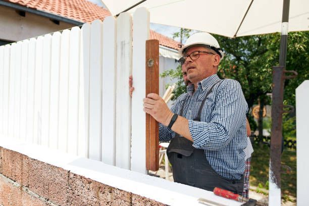 A senior contractor using a level to measure white wooden timber for a fence repair.