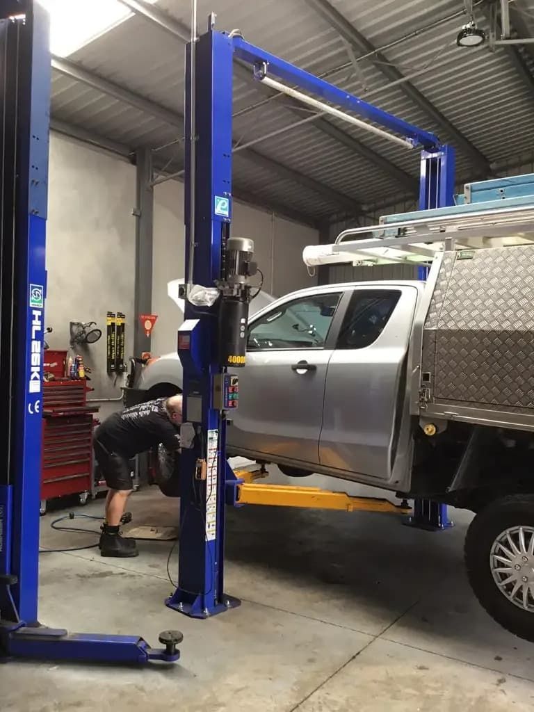 A Man is Working on a Truck on a Lift in a Garage — Auto Repair Solutions Unanderra In Unanderra, NSW