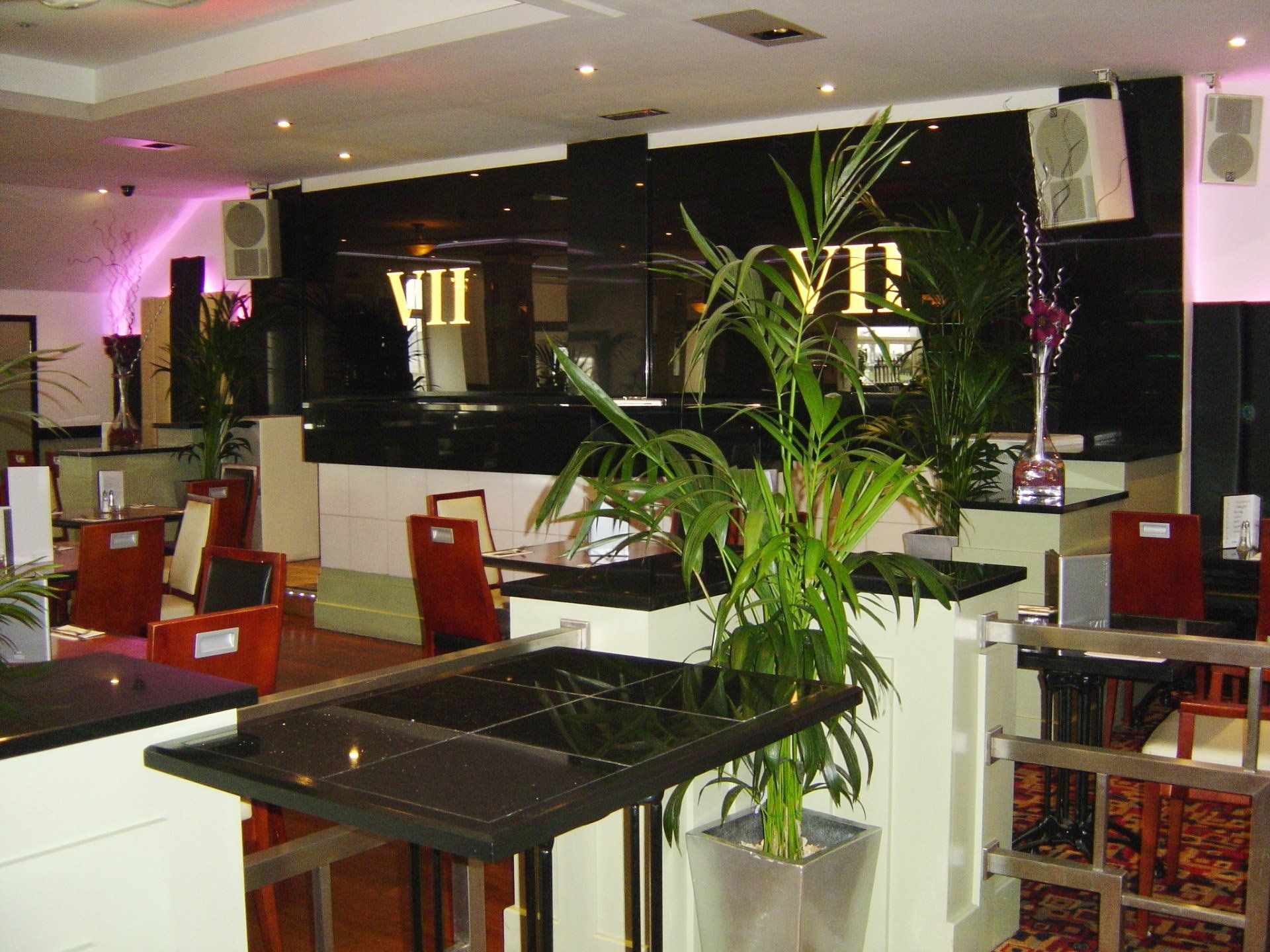 Interior of a restaurant, with tables and chairs. A black wall behind a counter with the word