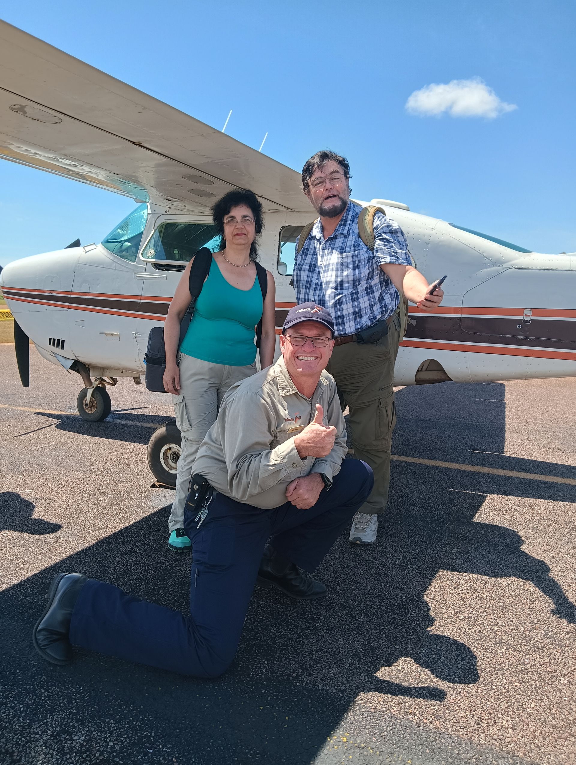 Three people pose near a small airplane on a sunny tarmac. One squats, giving a thumbs up — NT Driver Guide - Escorted Tours & Transfers in Darwin City, NT