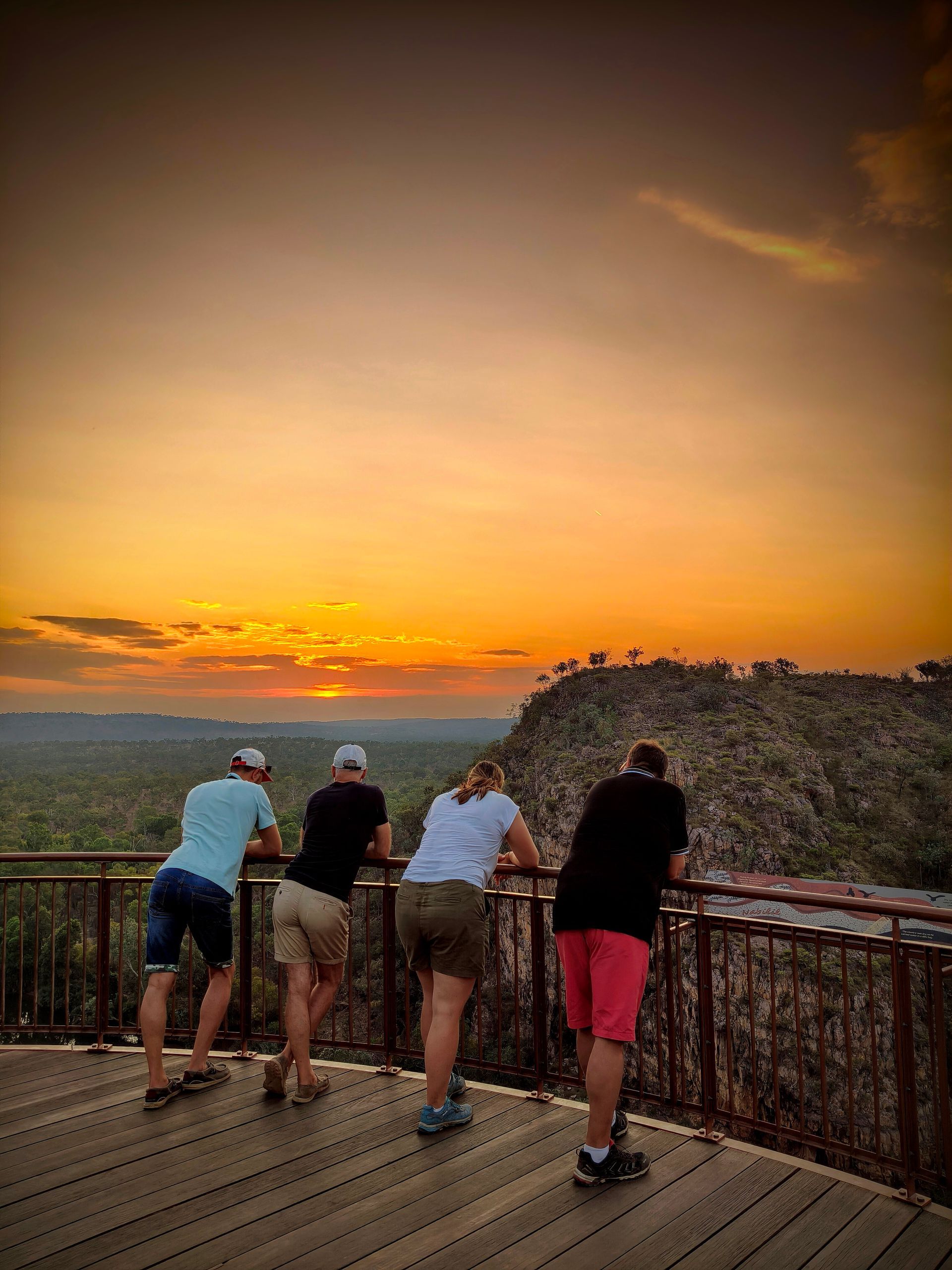 Four people watch the sunset over a landscape from a wooden deck with a railing — NT Driver Guide - Escorted Tours & Transfers in Darwin City, NT