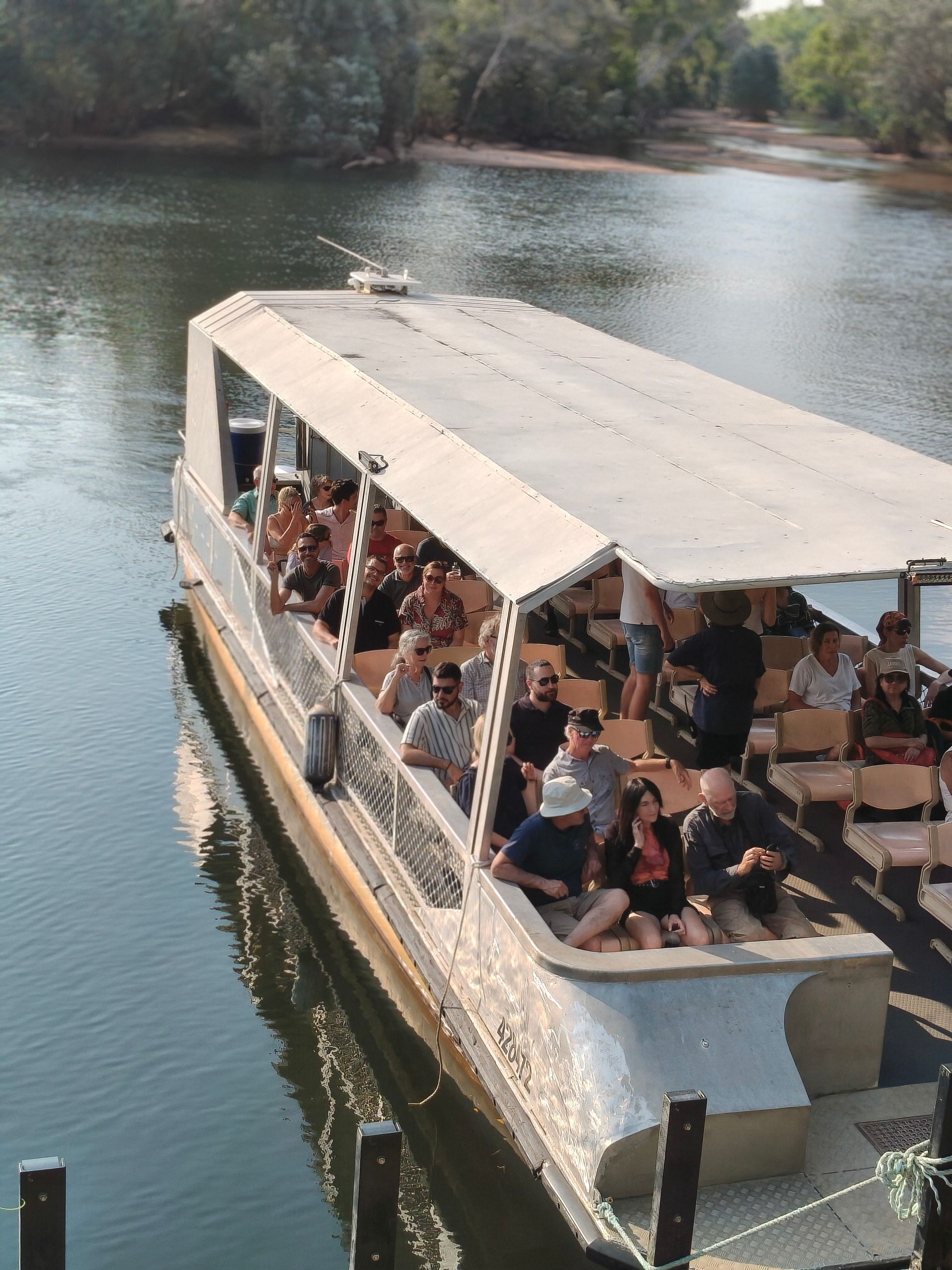Boat with passengers on a river; people sit and stand on the vessel — NT Driver Guide - Escorted Tours & Transfers in Darwin City, NT