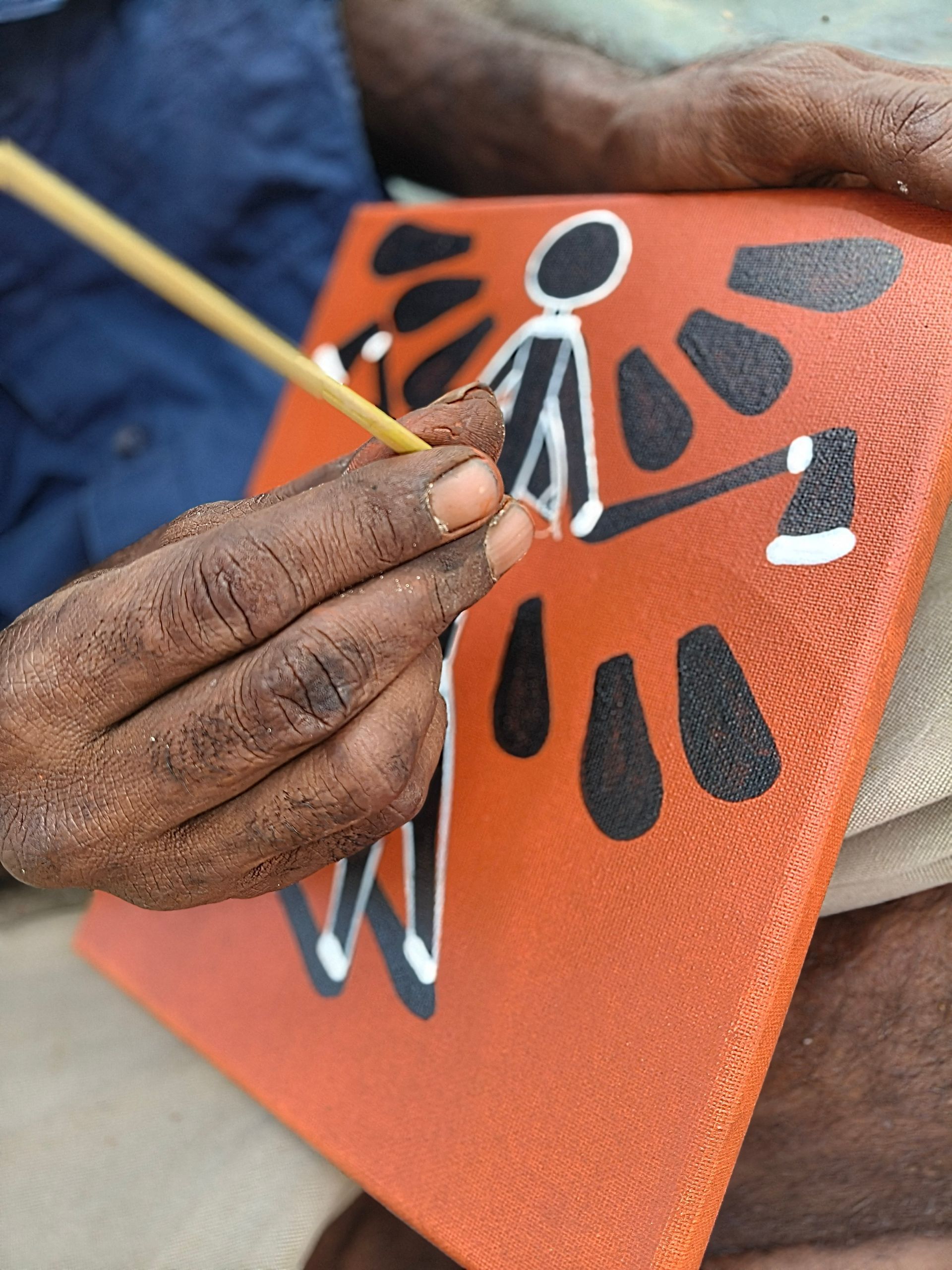 A person painting an abstract figure on an orange canvas with black and white shapes — NT Driver Guide - Escorted Tours & Transfers in Darwin City, NT