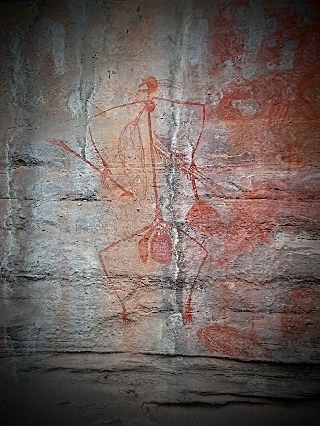Red rock art figure, arms outstretched, legs bent, on a weathered stone surface — NT Driver Guide - Escorted Tours & Transfers in Darwin City, NT
