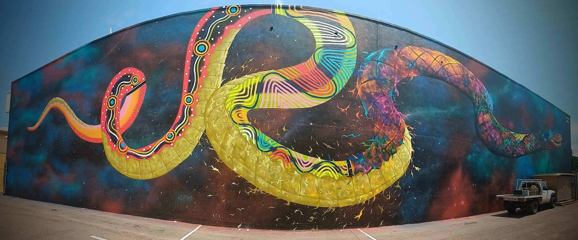 Large mural of a colourful snake with geometric patterns, on a long, curved wall — NT Driver Guide - Escorted Tours & Transfers in Darwin City, NT