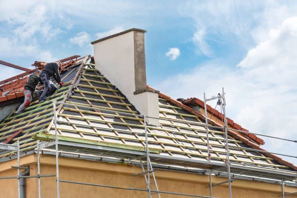 Workers performing re-roofing on a house with scaffolding and chimney under a partly cloudy sky.