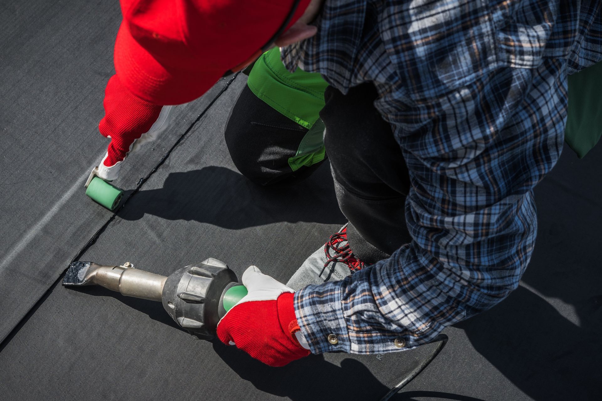 Roofer uses a hot air blower and roller to stick a rubber membrane to a roof.